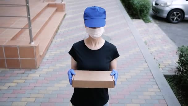 Postman, delivery man in protective mask and medical gloves carry small box parcel. Delivery service under quarantine, pandemic conditions. Social distancing concept - Video