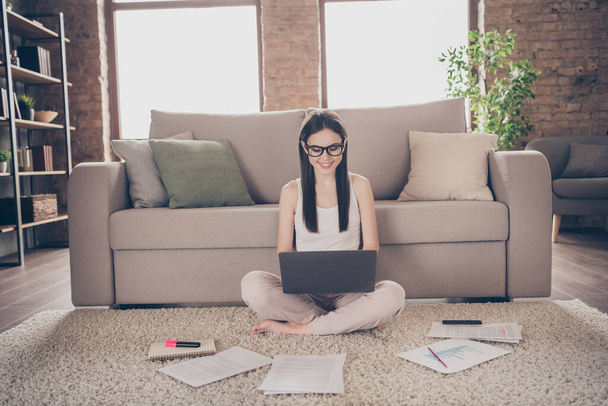 Full size photo of positive confident girl sit carpet legs crossed folded work distance laptop reading startup development progress presentation chatting executive collars in house indoors - 写真・画像