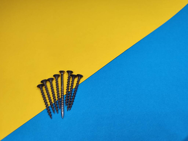 Black self-tapping screws with one white self-tapping screw on a yellow-blue background with copy space.The concept of relationships, the white crow. - Foto, Bild