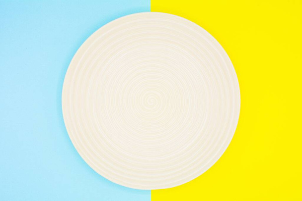 white ceramic dish on blue and yellow paper - background - Foto, Imagem