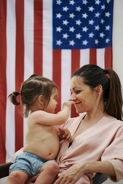 Una giovane donna seduta con la figlia con la bandiera americana sullo sfondo. Il concetto di America
 - Foto, immagini