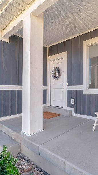 Marco vertical Sillas de porche blancas contra ventana y puerta principal del hogar con pared exterior gris
 - Foto, imagen