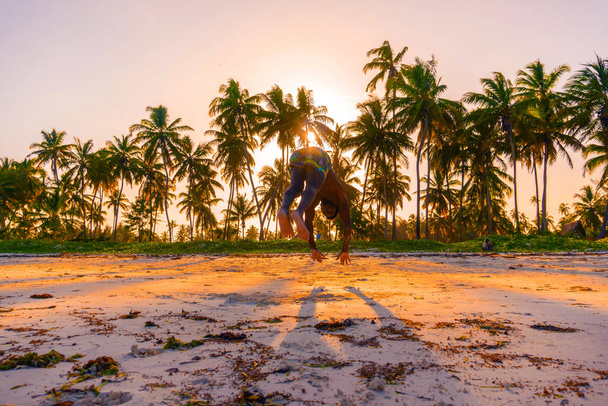 Jeune homme africain noir athlétique musclé et fort au White Sand Beach Training Acrobaties et gymnastique sautante Performance à la plage à l'heure du coucher du soleil
 - Photo, image
