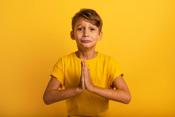 Child is pleading because he has something to request. Yellow background - Photo, Image
