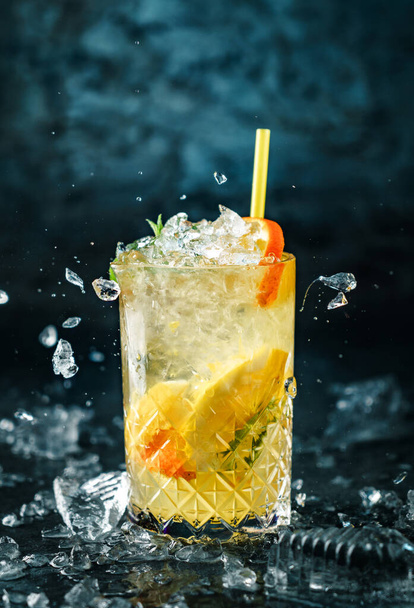 Δροσερή λεμονάδα με μέντα, τζίντζερ, πορτοκάλι και πάγο σε γυάλινο βάζο στο σκούρο μπλε φόντο. Στιγμιότυπο από ποτό σε παγωμένη κίνηση, ιπτάμενος πάγος, σταγόνες σε υγρό παφλασμό. Θερινό κρύο ποτό και κοκτέιλ - Φωτογραφία, εικόνα