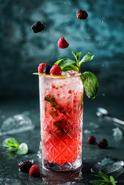Свіжі ягоди коктейлю з малиною, ожиною, м'ятою та льодом у склянці в банці на темно-синьому фоні. Студійний знімок напою під час заморожування, льотних крапель та ягід. Літній холодний напій і коктейль
 - Фото, зображення