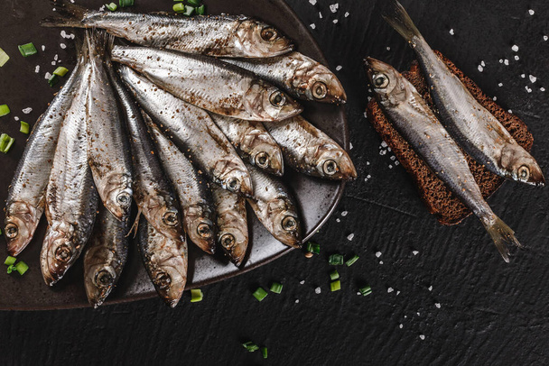 Sózott halak spratt pácolt fűszerek, só a tányéron át sötét kő háttér. Mediterrán ételek, előétel, tenger gyümölcsei, felső nézet - Fotó, kép
