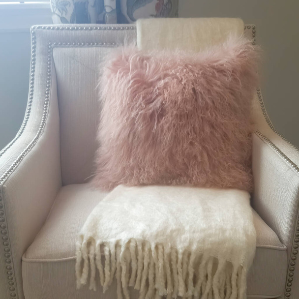 Almofada de lançamento peludo rosa quadrada e cobertor branco macio na poltrona dentro de um quarto
 - Foto, Imagem