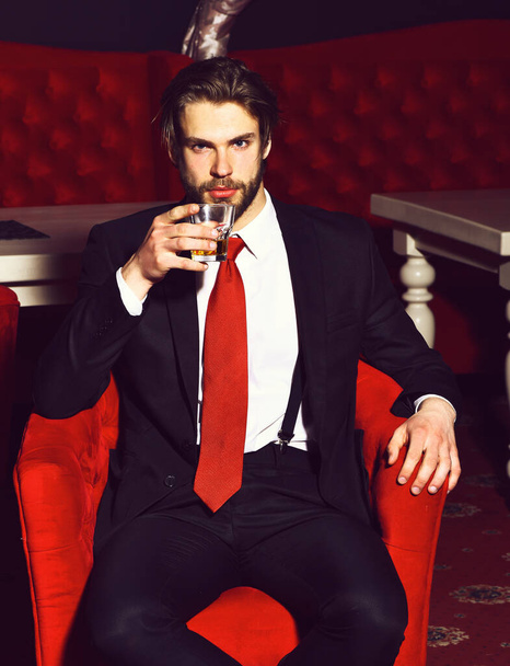 bearded man, businessman holding glass of whiskey in red chair - Фото, зображення