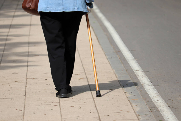 Woman walking with a cane on a street, female legs on pavement. Concept for disability, limping person, diseases of the spine, old people - Foto, Bild