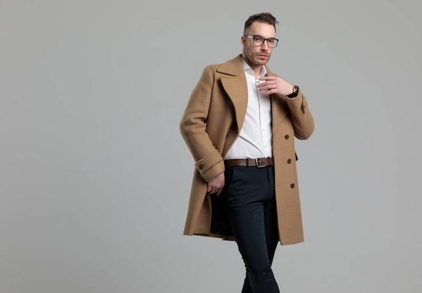 眼鏡と長いコートを身に着けているセクシーな若いファッションモデル,灰色の背景に立って - 写真・画像