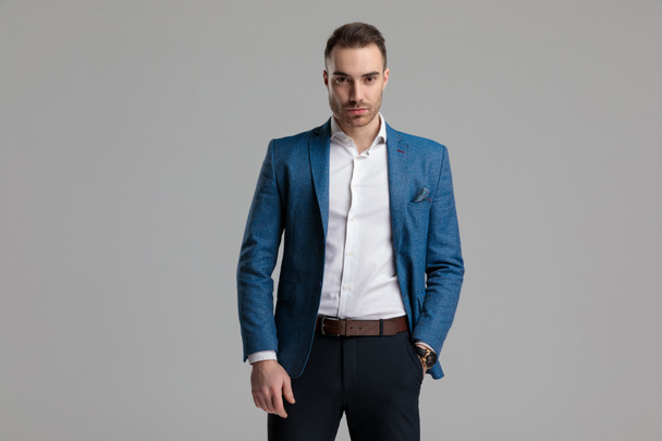 сексуальный молодой умный мужчина держит руку в кармане и позирует, стоя на сером фоне
 - Фото, изображение