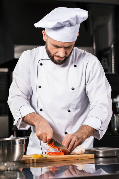 Chef man with knife at restaurant kitchen. Chef male slicing pepper. - Foto, Imagem