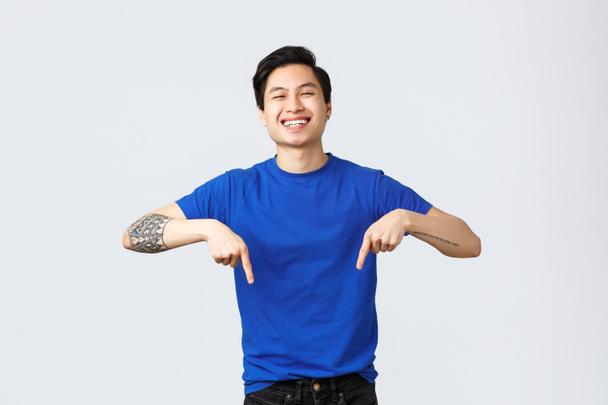 Different emotions, people lifestyle and advertising concept. Carefree good-looking male student in blue t-shirt, pointing fingers down, smiling delighted, introduce new product or banner - Photo, Image