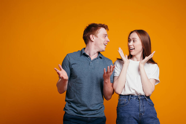The red-haired guy tells his girlfriend good news and she enjoys a sudden surprise on an orange background in the studio - Φωτογραφία, εικόνα