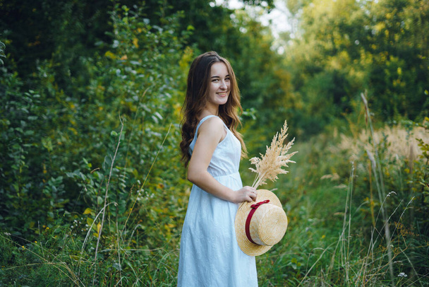Kaunis tyttö valkoisessa mekossa, jossa on kukkakimppu. Nuori nainen vihreässä puistossa. Tyttö mekko ja kesän aurinkoinen päivä - Valokuva, kuva