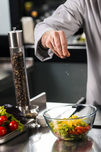 Šéfkuchař nasoloval salát v restauraci. Detailní samec ručně solená zelenina. - Fotografie, Obrázek