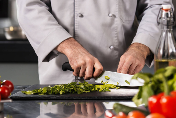 Man hands cut food at kitchen. Closeup chef hands cutting vegetables with knife. - Photo, image