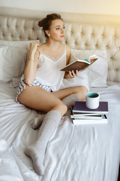 Onnellinen nuori woomen rentouttava sängyllä ja lukeminen kirja pysyä kotona. Tyttö oppii kotona käsittelyssä kirjallisuutta karanteenin aikana - Valokuva, kuva