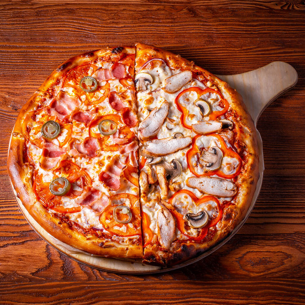 Delicious round pizza on a wooden stand on the table - Фото, изображение