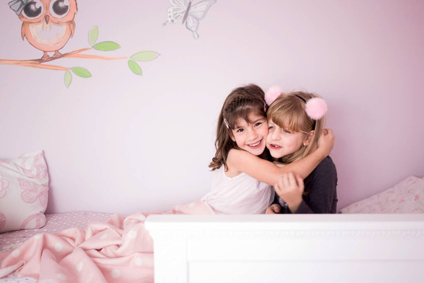 Adorable, lindo, niñas, hermanas, gemelas abrazándose en la cama en su encantadora habitación rosa - Foto, imagen