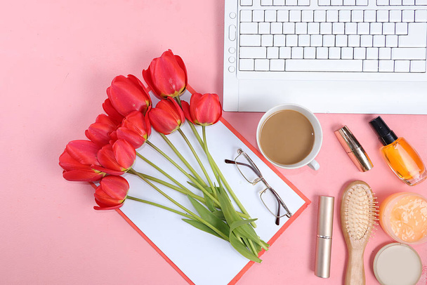 Work desk of a modern woman, home office. Notepad, tea, spring flowers and cosmetics on a light table. Minimal business concept, flat lay, place for text. - Photo, image
