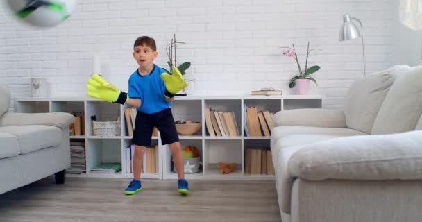 Een jongen van zes die voetbal speelt met handschoenen van keeper 's thuis tijdens quarantaine COVID-19. Levensstijl in het appartement. 4k - Video