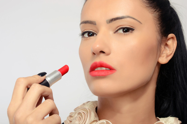 Portrait of a beautiful brunette woman applying red lipstick - 写真・画像