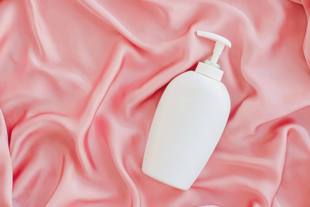 Etiqueta en blanco botella de envase cosmético como maqueta del producto sobre fondo de seda rosa
 - Foto, imagen