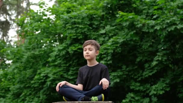 Dziecięca joga w parku. Młody chłopiec w pozycji do jogi zamknij oczy i medytuj. - Materiał filmowy, wideo
