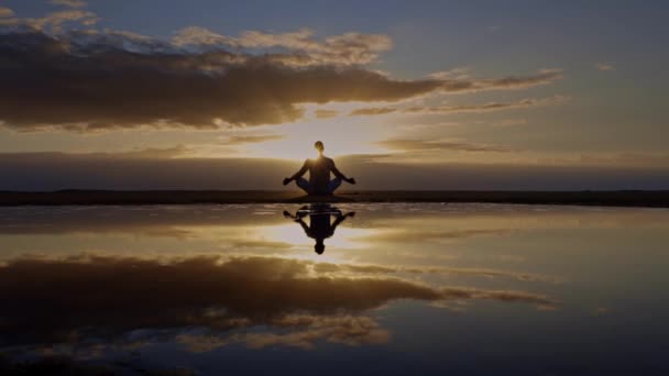 yoga méditation silhouette lotus lever de soleil plage, pleine conscience, concept de bien-être et de bien-être, réflexion de l'eau de l'homme dans la pose de lotus de yoga assis seul sur le sable avec fond nuage océan, espace de copie - Séquence, vidéo