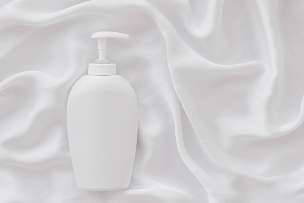 Etiqueta en blanco botella de envase cosmético como maqueta del producto sobre fondo de seda blanca
 - Foto, imagen