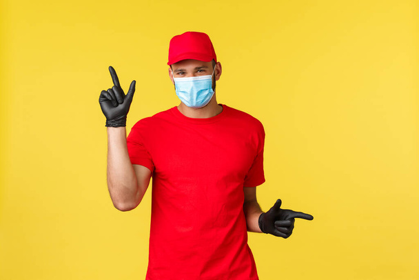 Express delivery during pandemic, covid-19, safe shipping, online shopping concept. Smiling cute courier in medical mask provide options for contactless package transfer, pointing left and right - Fotó, kép