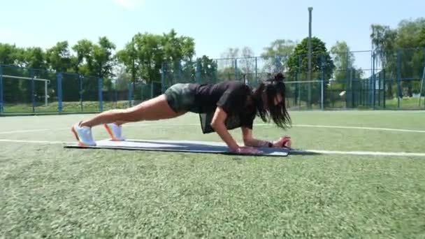 Fitness woman in sportswear doing various exercises on sports mat, on green football field with white markings, at stadium. Outdoor sports. online training. hot summer day. healthy lifestyle concept - Materiał filmowy, wideo