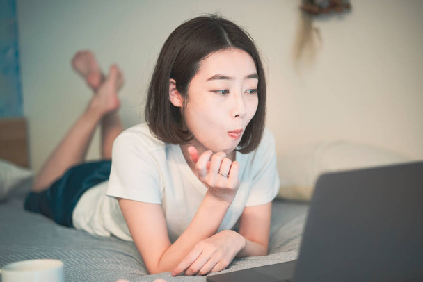 Азиатская молодая женщина смотрит на экран ноутбука в комнате дома
 - Фото, изображение