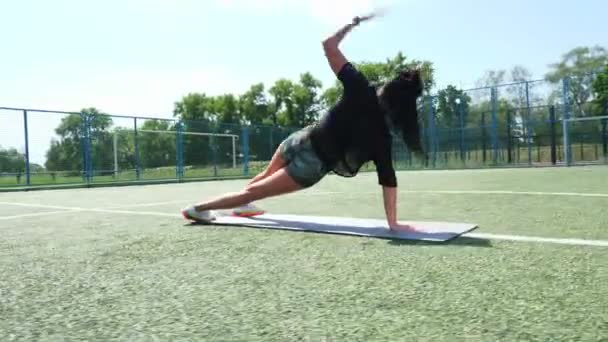 Fitness woman in sportswear doing various exercises on sports mat, on green football field with white markings, at stadium. Outdoor sports. online training. hot summer day. healthy lifestyle concept - Video