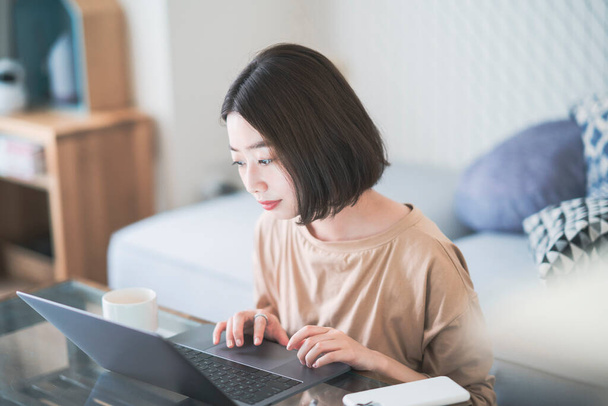 Ασιάτισσα νεαρή γυναίκα επικοινωνεί online χρησιμοποιώντας το laptop στο σπίτι - Φωτογραφία, εικόνα