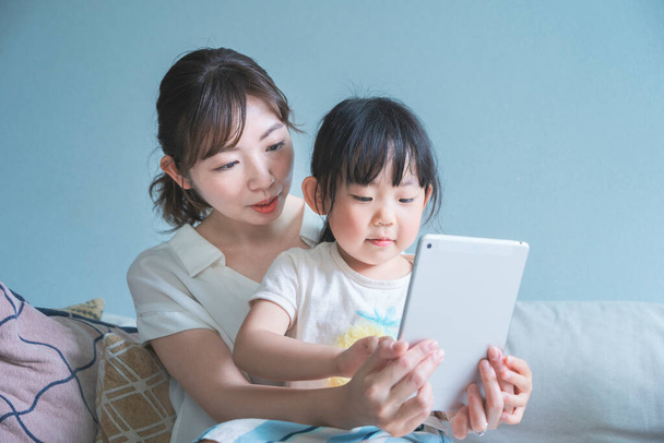 Mãe e filha sentadas em um sofá e operando um dispositivo tablet
 - Foto, Imagem
