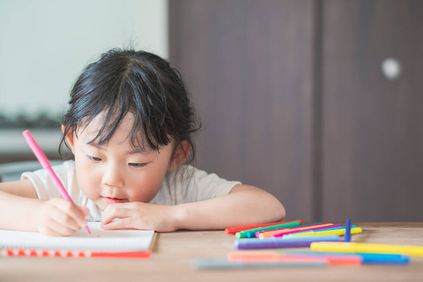 Азиатская девушка рисует красочными ручками за обеденным столом дома
 - Фото, изображение