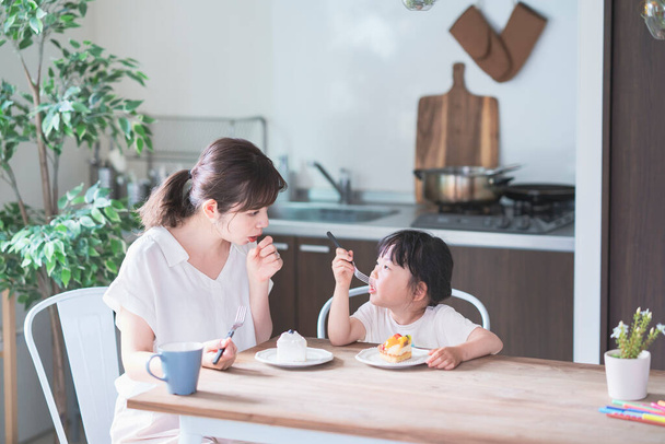Азиатские мама и дочь едят торт за обеденным столом дома
 - Фото, изображение
