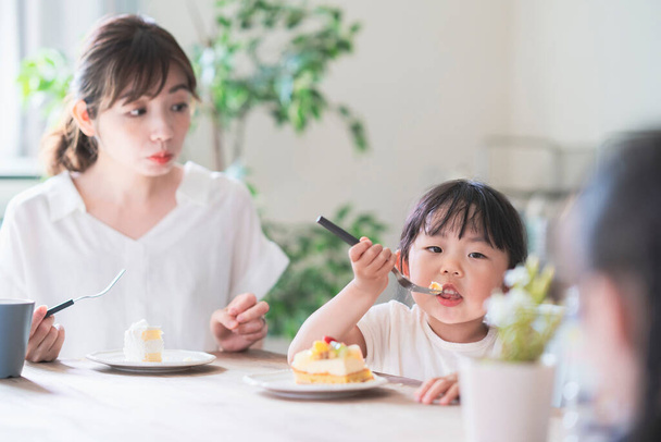 Asyalı anne ve kızı evdeki yemek masasında pasta yiyorlar. - Fotoğraf, Görsel