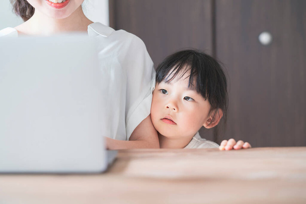 Asian little girl snuggling up to mom teleworking at home - Photo, Image