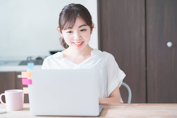 Femme asiatique faisant du travail à distance avec ordinateur portable à table à manger à la maison - Photo, image