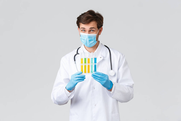 Kórház, egészségügyi dolgozók, kovid-19 kezelési koncepció. Laboratóriumi technikus próbálja megtalálni a koronavírus vakcinát, ampullákat mutat mintákkal, orvosi maszkot és köpenyt visel - Fotó, kép