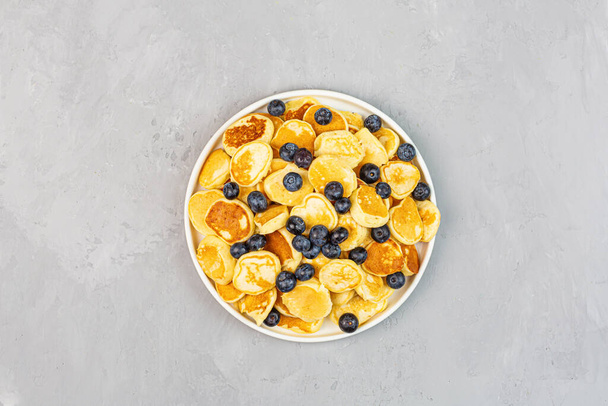 Trendy home breakfast with tiny pancakes and blueberry on gray concrete background. Flat lay, top view, overhead, mockup, template, copy space. View from above - Photo, Image