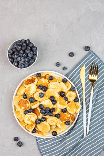 Trendy home breakfast with tiny pancakes and blueberry on gray concrete background. Flat lay, top view, overhead, mockup, template, copy space. View from above - Fotó, kép
