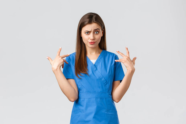 Медицинские работники, предотвратить вирус, страхование и медицина концепции. Забавная недовольная медсестра в синих халатах гримасирует, волнуется из-за чего-то, имитирует и смотрит в камеру в шоке
 - Фото, изображение