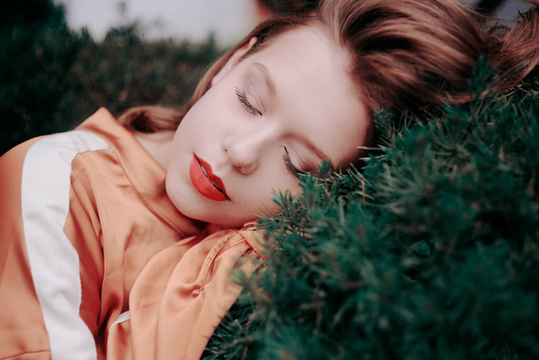 Chic bellissimo modello su uno sfondo di legno, natura, verde, abete rosso. Ragazza con i capelli corti e un vestito marrone La bionda è sdraiata su un albero, il sonno
 - Foto, immagini