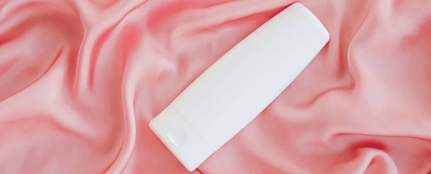 Etiqueta en blanco botella de envase cosmético como maqueta del producto sobre fondo de seda rosa
 - Foto, Imagen