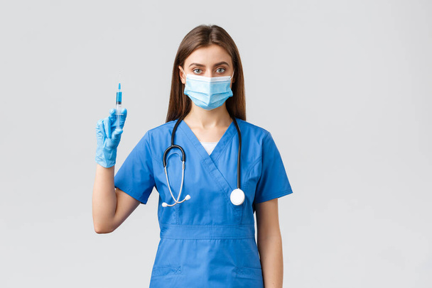 Covid-19 、ウイルス、健康、医療従事者および検疫の概念を防止する。青い頭蓋骨の深刻な女性看護師、医師コロナウイルスワクチンと医療マスク保持注射器を身に着けています - 写真・画像